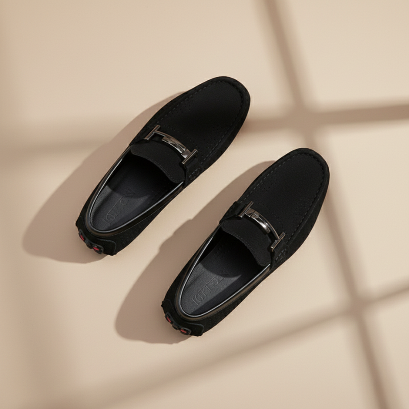 Pair of black loafers with silver buckles on a beige background