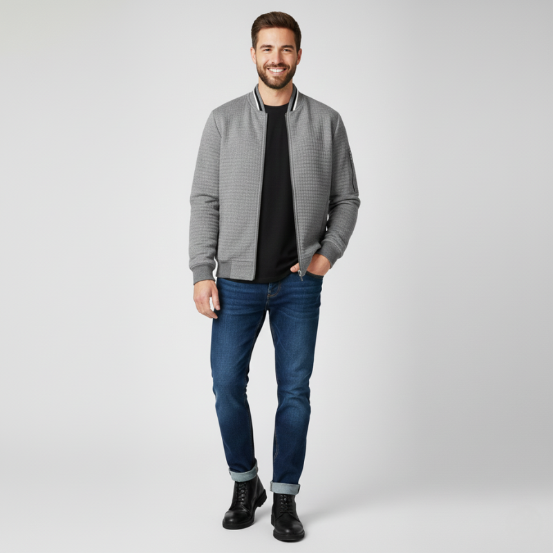 Man wearing a gray checkered bomber jacket, black t-shirt, blue jeans, and black boots on a white background