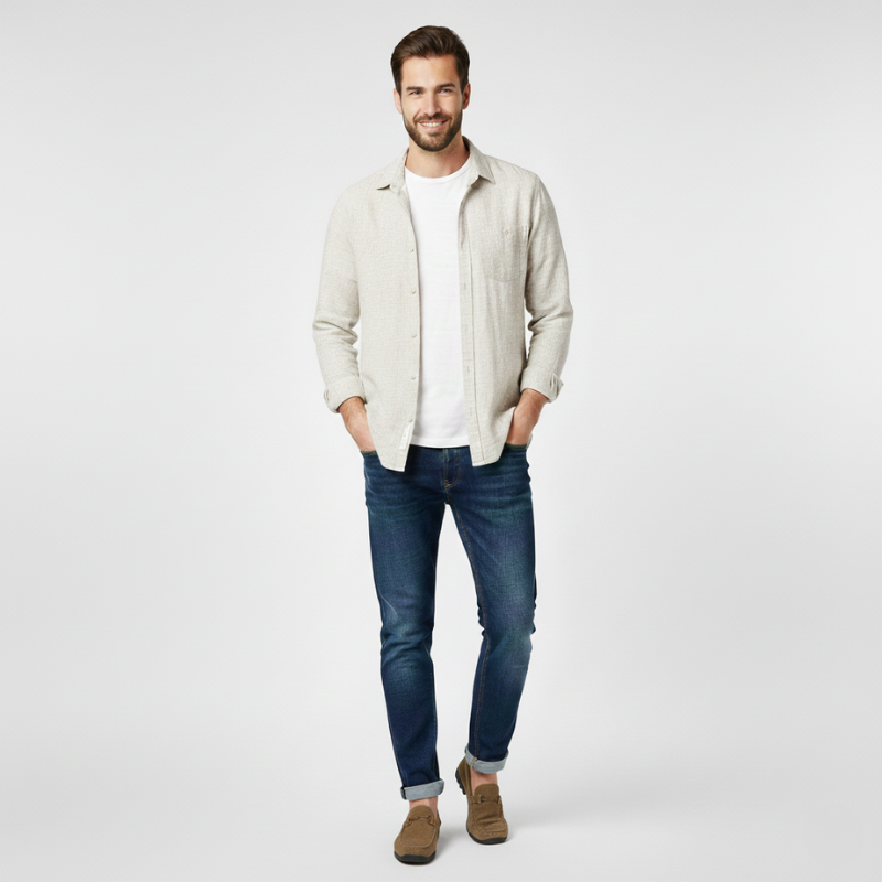 Man wearing a beige jacket, white shirt, blue jeans, and brown shoes on a light gray background