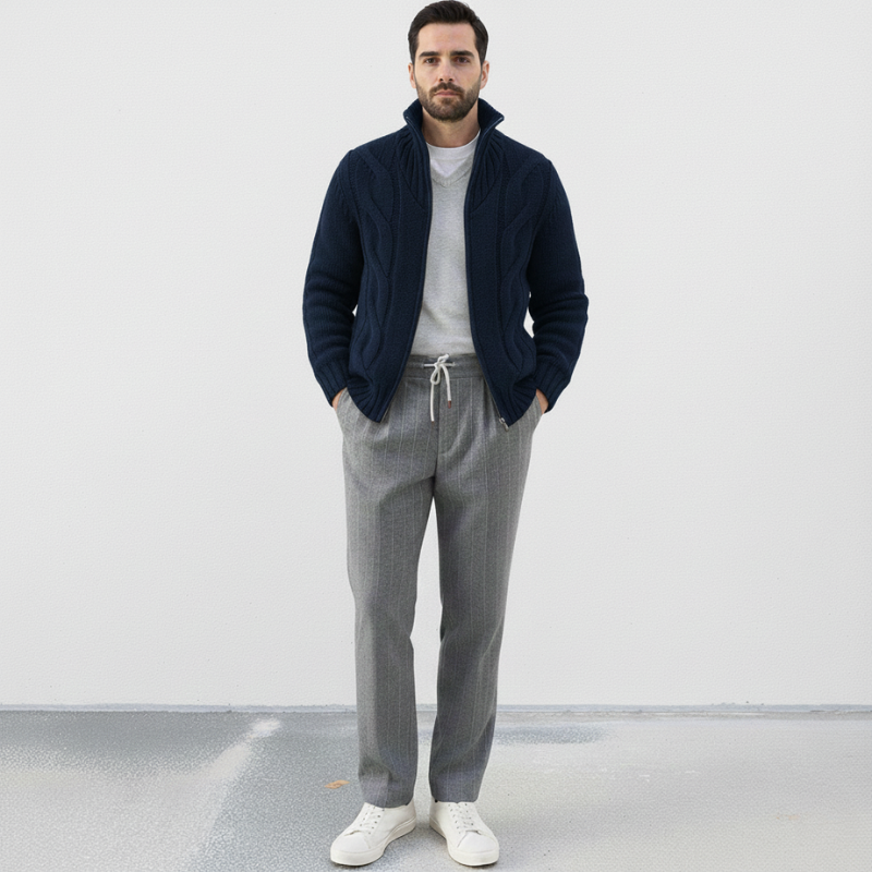 Man wearing a navy jacket, gray pants, and white shoes on a plain background