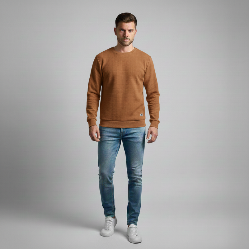 Man wearing a brown sweater and blue jeans on a gray background
