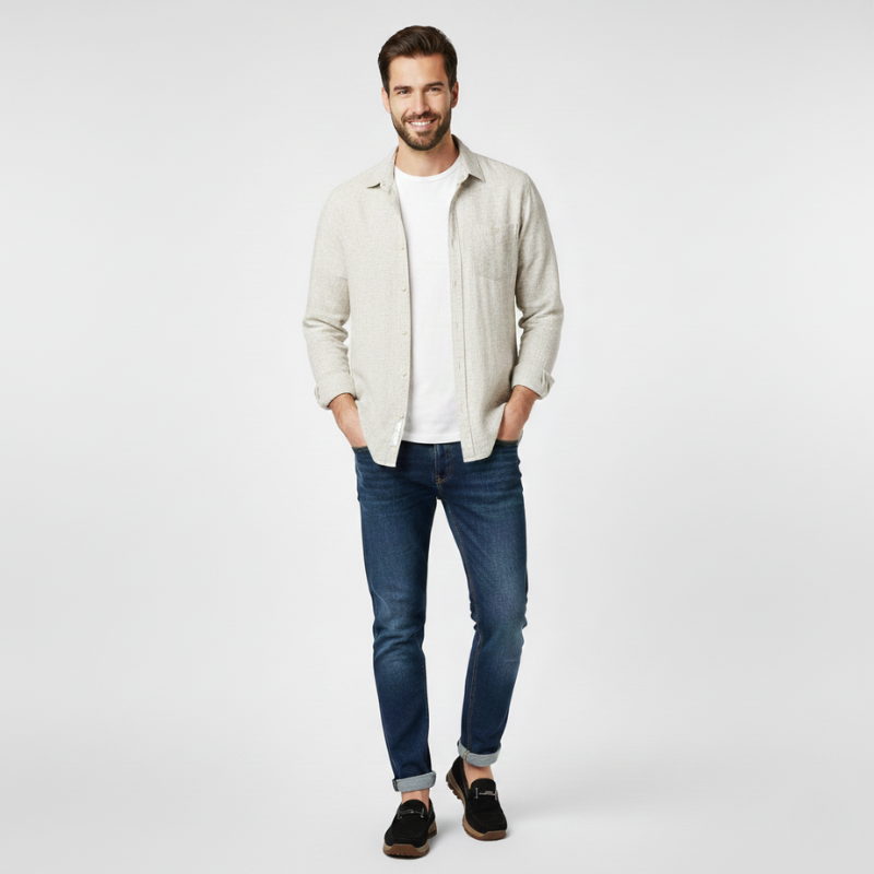 Man wearing a light-colored jacket, white shirt, blue jeans, and dark shoes on a plain background