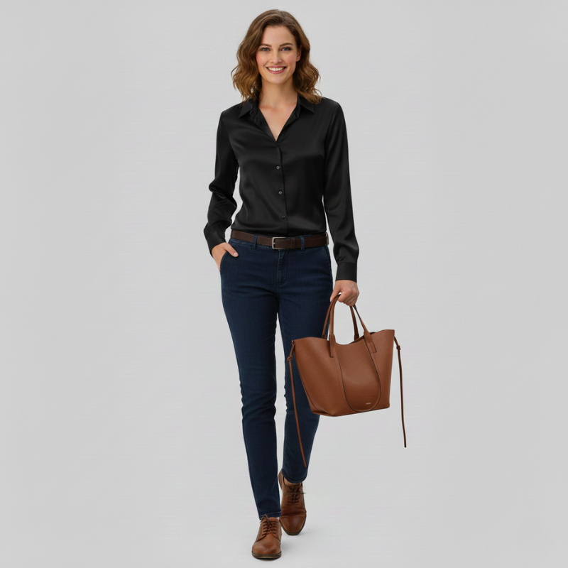 Woman wearing a black shirt, blue jeans, and brown boots holding a brown handbag on a gray background