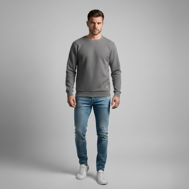 Man wearing a gray sweater and blue jeans on a gray background