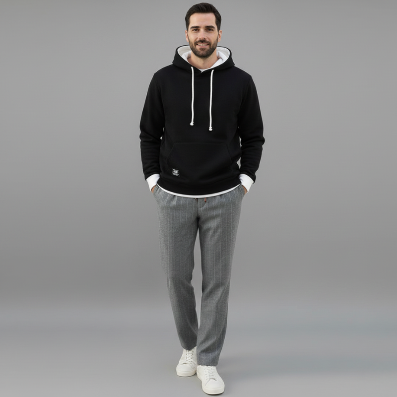 Man wearing a black hoodie, gray pants, and white sneakers on a gray background