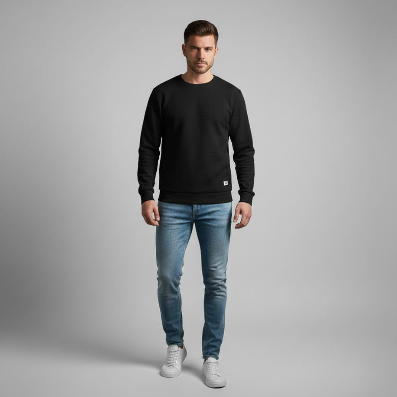 Man wearing a black sweatshirt, blue jeans, and white sneakers on a gray background