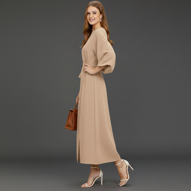 Woman wearing a beige maxi dress standing in a minimalist studio.