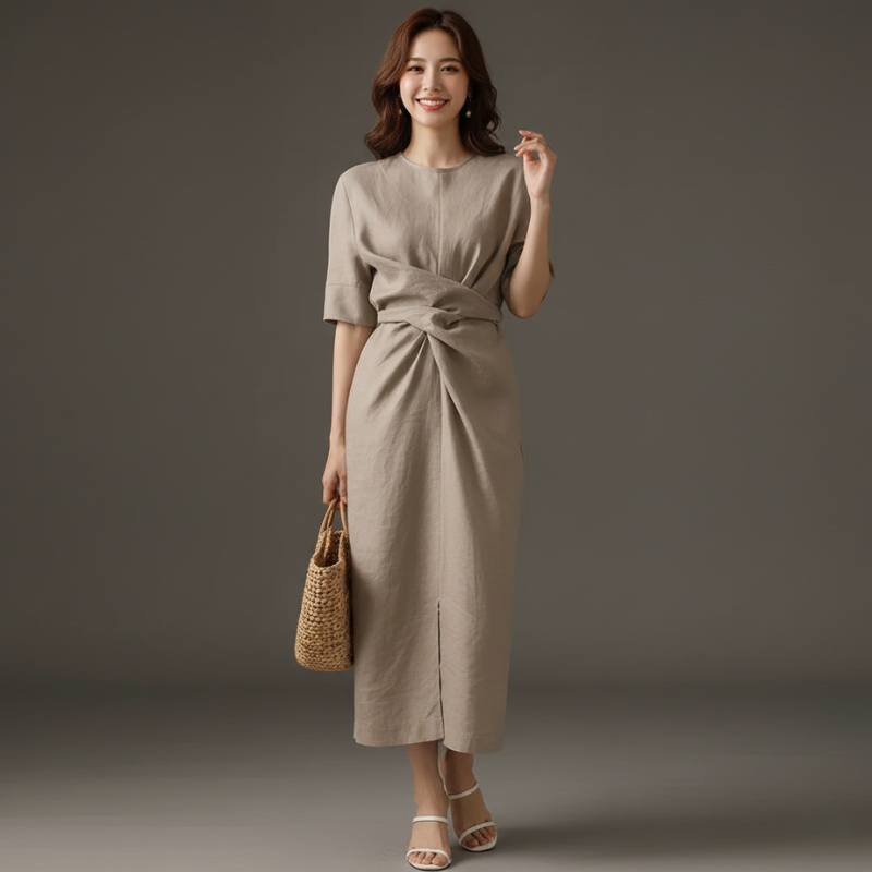 Woman wearing a beige midi dress with side draping standing in a studio.