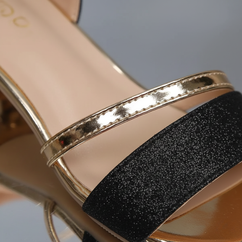 Close-up of a sandal with gold strap and black glittery band on a light gray background