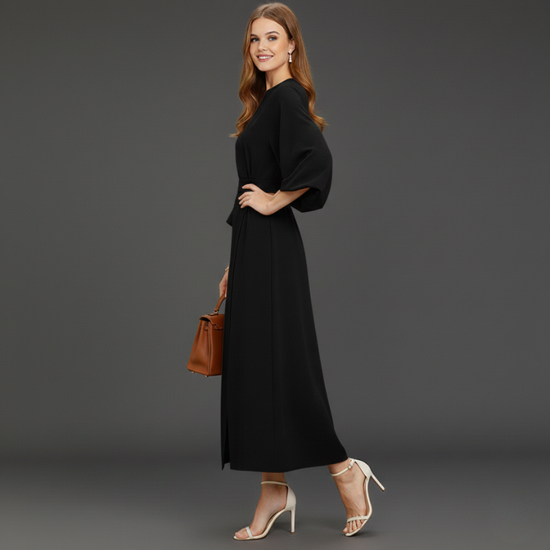 Woman wearing a black maxi dress posing in a dark grey studio.