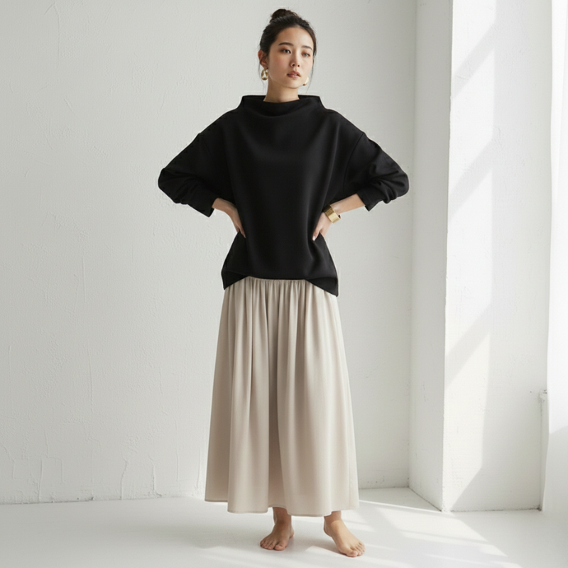 Person wearing a black sweater and beige skirt in a minimalistic setting