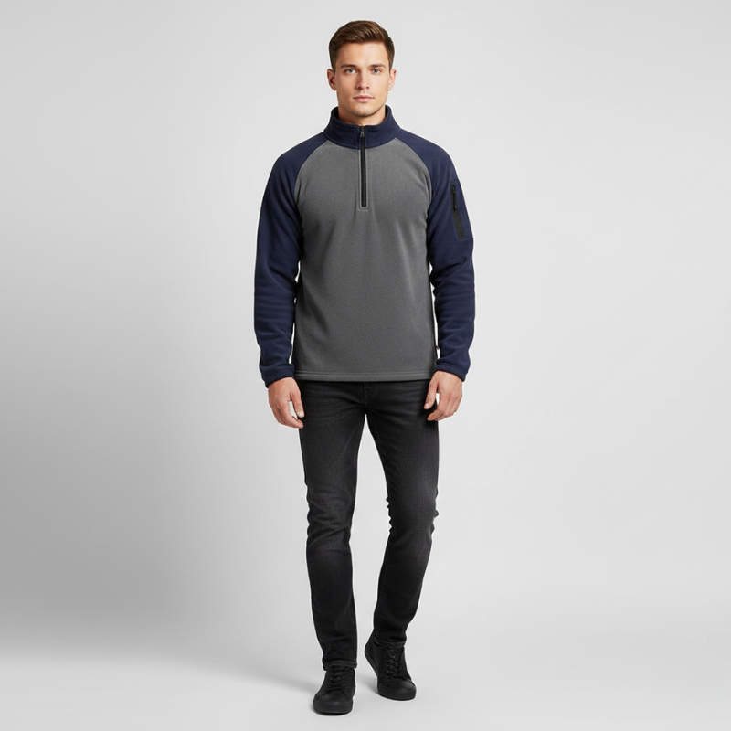 Man wearing a gray and navy pullover with black pants on a light gray background