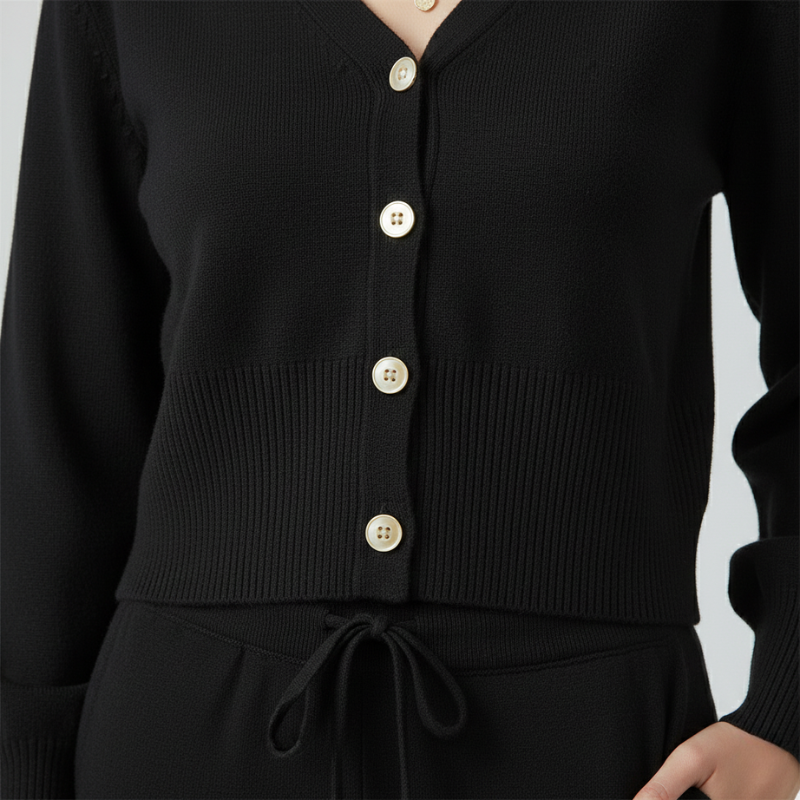 Black cardigan with gold buttons on a plain background