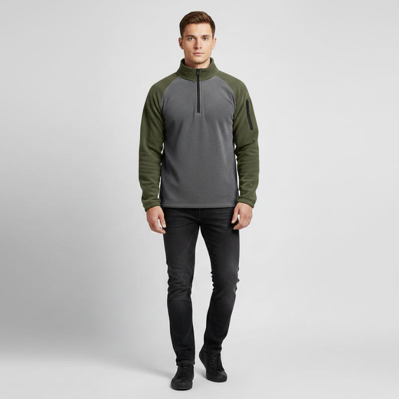 Man wearing a green and gray pullover with black pants on a light gray background