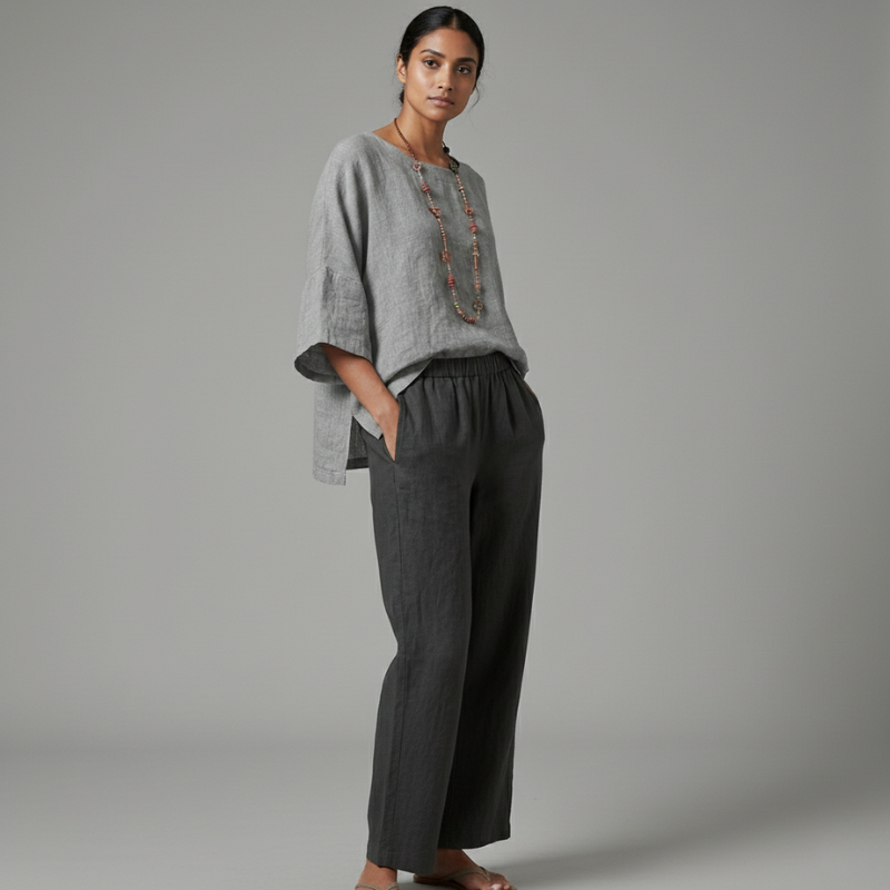 Woman wearing a gray top and dark gray pants against a plain background