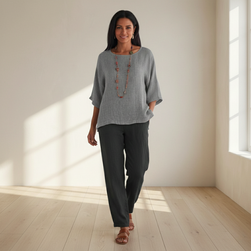Woman wearing a gray top and black pants in a bright room with sunlight streaming in.