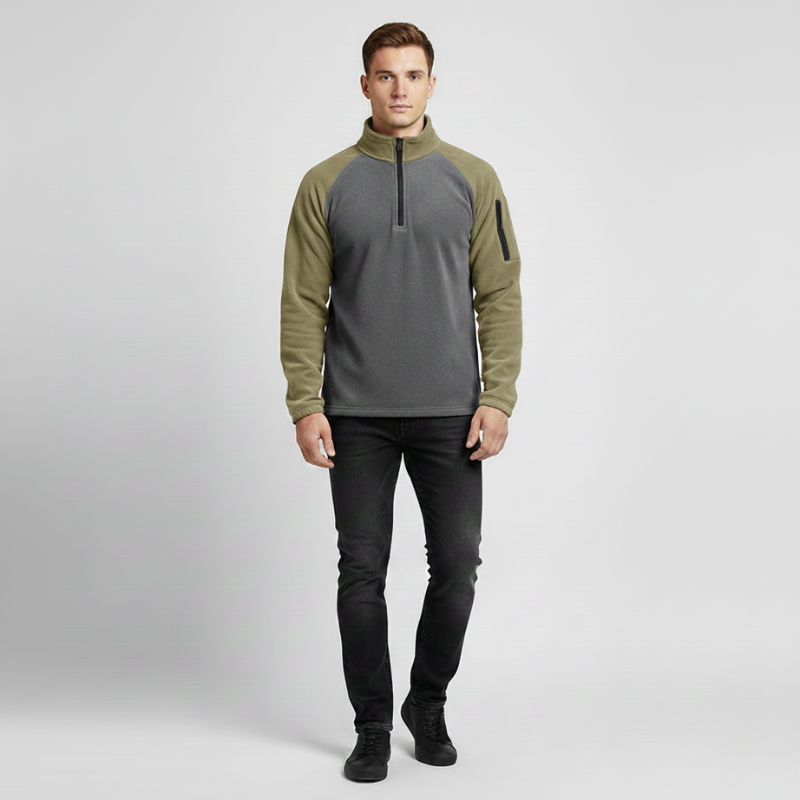 Man wearing a green and gray pullover with black pants on a light gray background