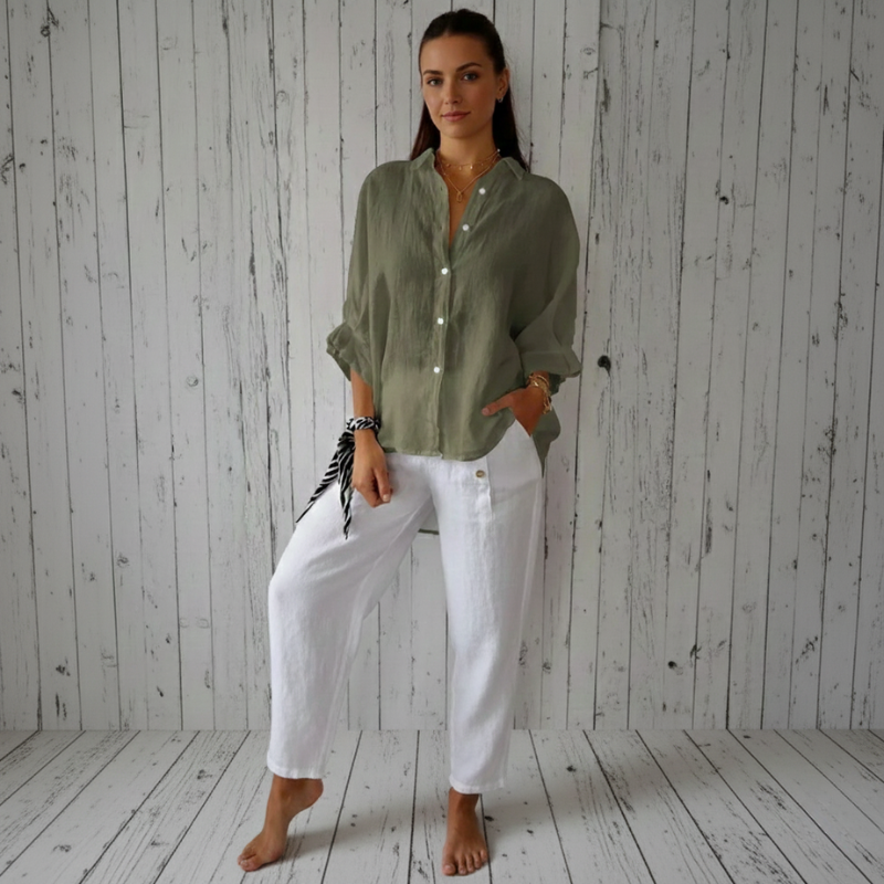 Woman wearing a green shirt and white pants standing against a wooden wall.