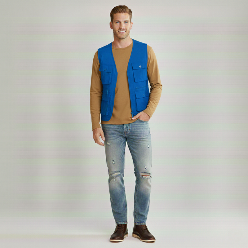 Man standing indoors wearing a navy casual vest styled with jeans and a button-up shirt.