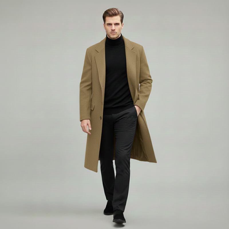 Man wearing a gray long wool overcoat styled with a black turtleneck and black trousers in a clean studio setting.