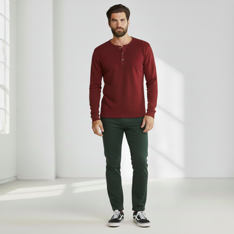 Man wearing a burgundy crew neck sweater paired with black pants in a bright studio setting.