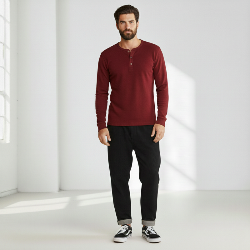 Man wearing a burgundy crew neck sweater paired with black pants in a bright studio setting.
