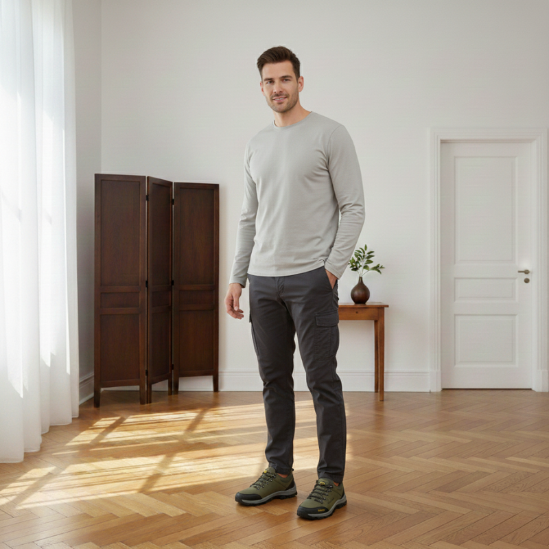 Man wearing olive hiking shoes styled with a light sweater and dark pants in an indoor setting.