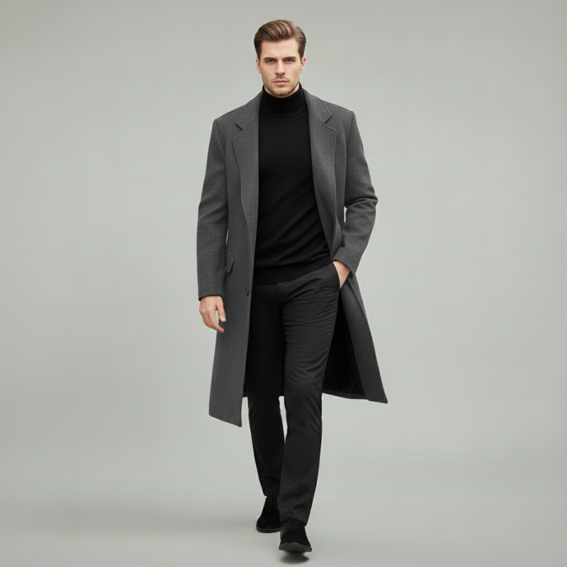 Man wearing a gray long wool overcoat styled with a black turtleneck and black trousers in a clean studio setting.