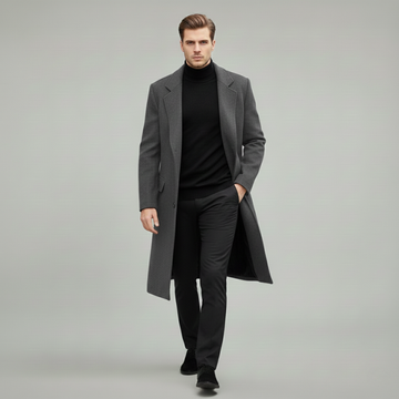 Man wearing a gray long wool overcoat styled with a black turtleneck and black trousers in a clean studio setting.