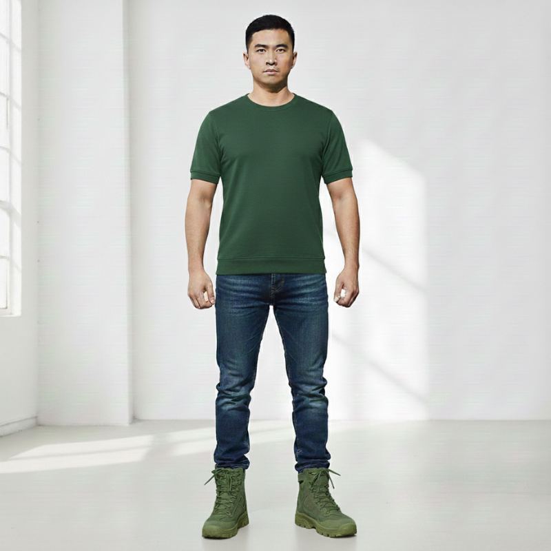 Man wearing a green crew neck t-shirt with blue jeans and casual shoes in a bright studio setting.
