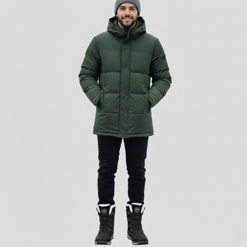 Man wearing a green outdoor jacket paired with dark pants and hiking boots in a studio setting.