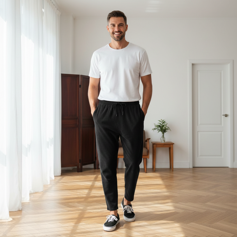 Man wearing a white t-shirt paired with black pants in natural indoor lighting.