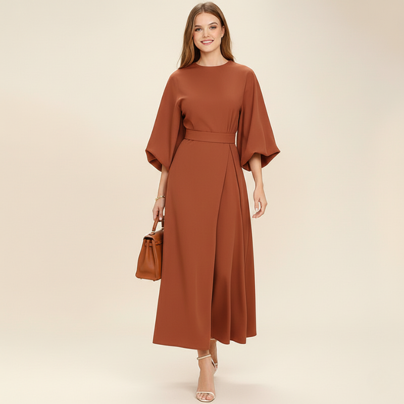 Model standing in a rust-colored maxi dress inside a styled studio.