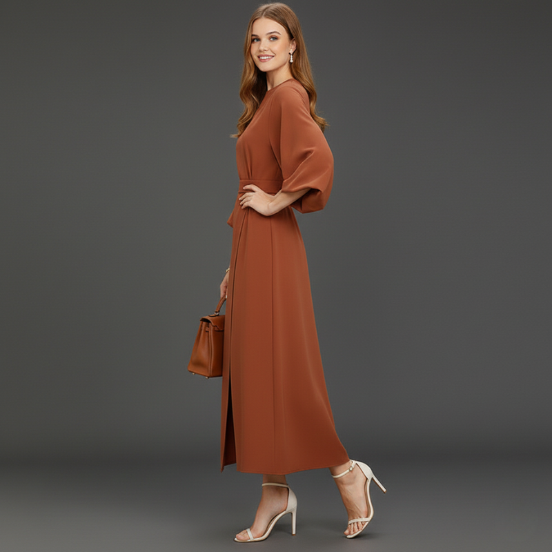 Model standing in a rust-colored maxi dress inside a styled studio.