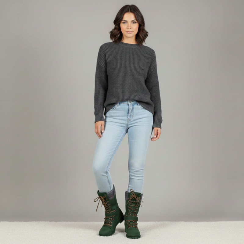 Woman wearing a dark gray sweater, light blue jeans, and green boots on a plain background