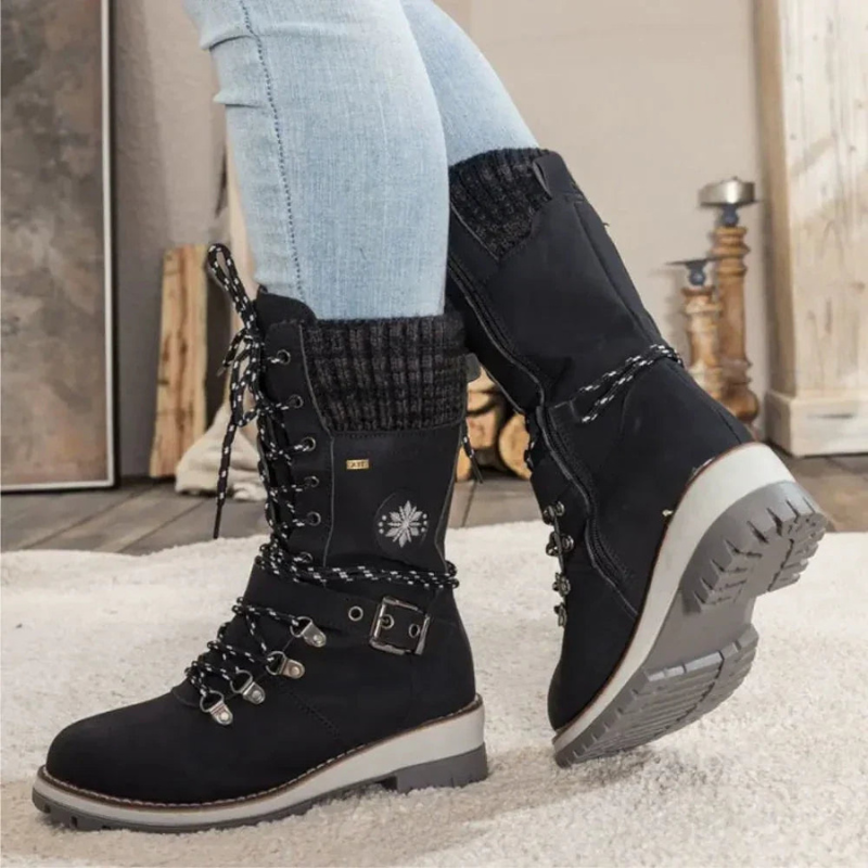 Black hiking boots with decorative elements worn by a person indoors.