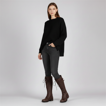 Woman wearing brown lace-up combat boots styled with a black sweater and gray skinny pants in a clean studio setting.