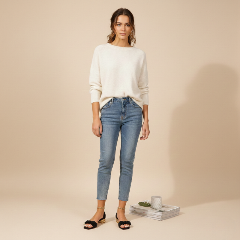 Woman wearing a white sweater and blue jeans standing against a beige background