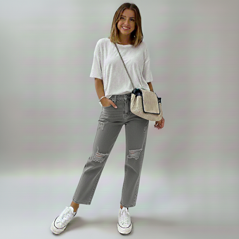 Woman wearing a white t-shirt, gray ripped jeans, and white sneakers with a beige crossbody bag on a plain background.