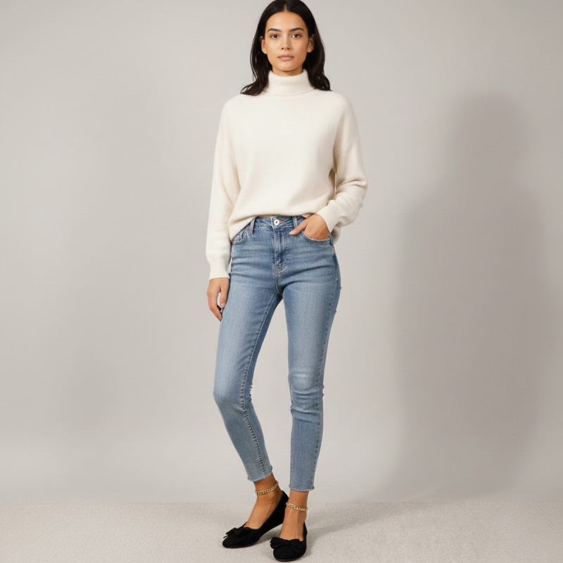 Woman wearing a white turtleneck sweater and light blue jeans on a gray background