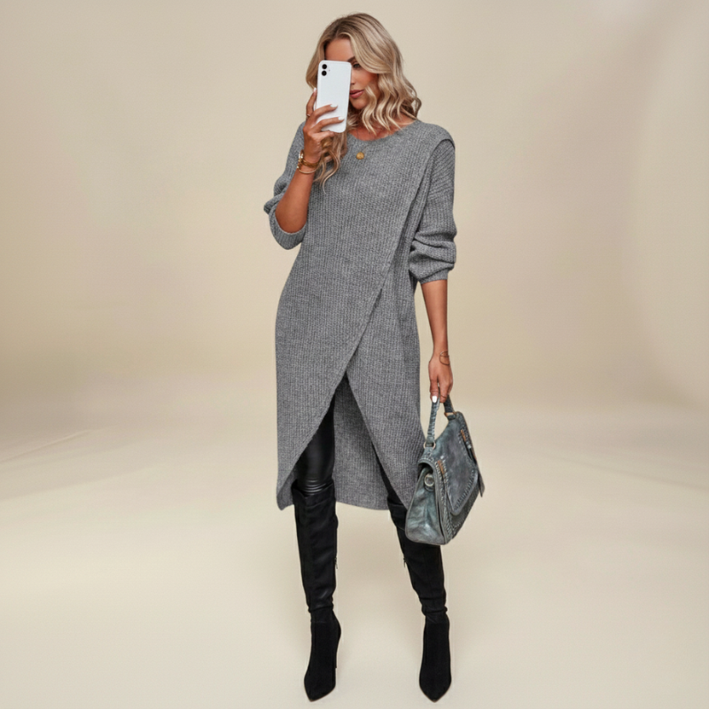 Woman wearing a gray sweater dress with black leggings and boots, holding a phone and a handbag on a beige background.