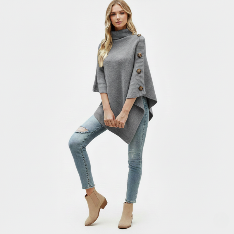 Woman wearing a gray poncho with button details, light blue jeans, and beige ankle boots on a white background.