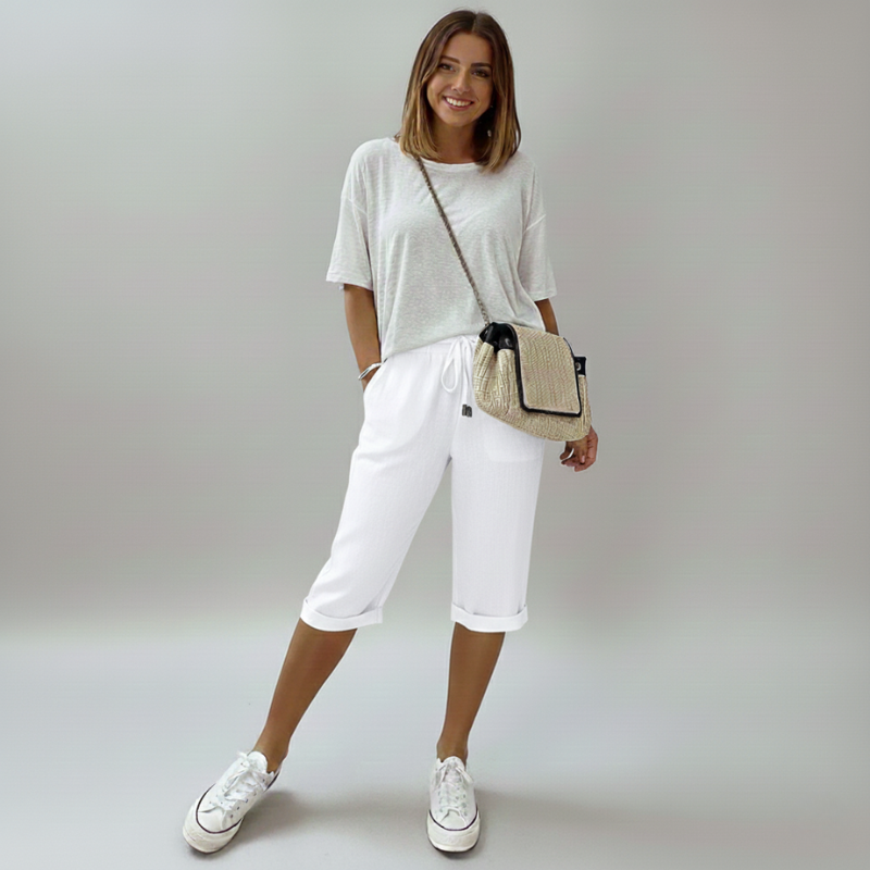 Woman wearing a white outfit with a beige bag on a plain background