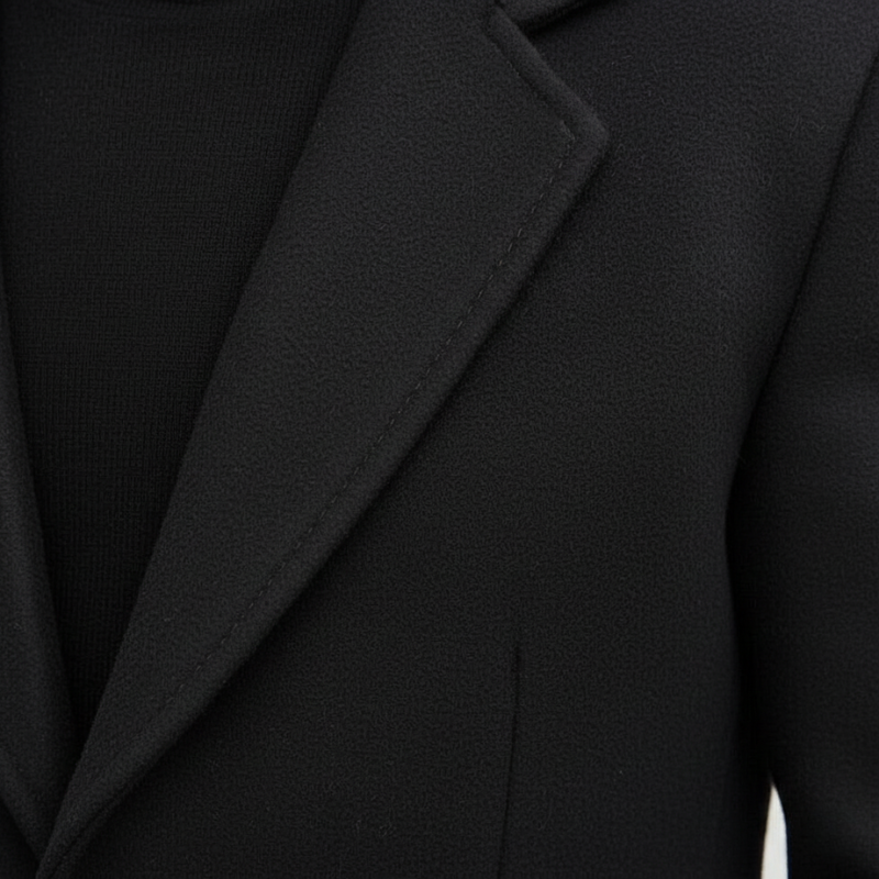 Close-up of a black wool overcoat showing sharp lapels, smooth fabric texture, and tailored stitching.
